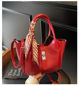 Detail view of red stone texture bucket bag featuring metal lock and decorative silk scarf