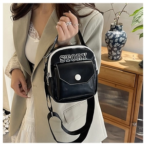 Détail du sac bandoulière noir et blanc avec imprimé STORY porté sur un blazer kaki