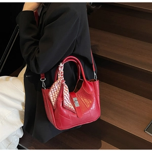 Detail of red croc-embossed bucket bag with a decorative silk scarf on a wooden staircase