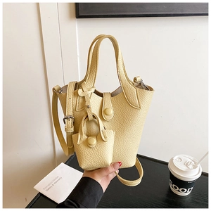 Detail of cream lychee texture leather bucket bag with mini charm and adjustable strap