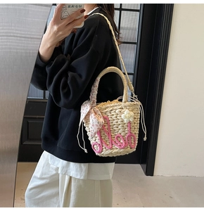 Mirror selfie showing woven straw bucket bag with floral scarf handle and pink embroidery