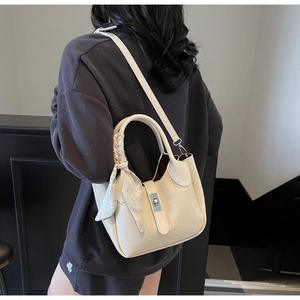 Detail of beige crocodile embossed bucket bag with silk scarf on handle and metal twist lock