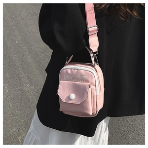 Détail d'un petit sac bandoulière rose en nylon avec poche avant et texte STORY