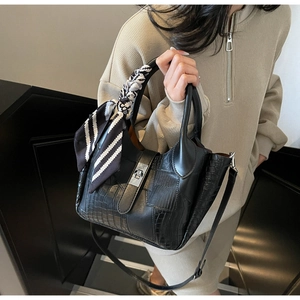 Detail of black leather bucket bag with crocodile texture and decorative silk scarf strap