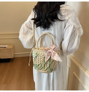 Detail of straw bucket bag with floral ribbon and green hello embroidery on a model