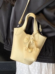 Beige lychee pattern bucket bag with mini charm accessory worn by a model