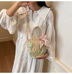 Detail of a straw bucket bag with green hello embroidery and a pink floral scarf tie