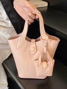 Pink pebbled leather bucket bag with matching mini charm shown in a handheld view