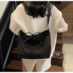 Detail of black canvas tote bag with drawstring bow and front pocket worn on stairs