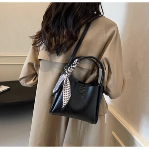 Detail of a black leather bucket bag with a patterned silk scarf on a female model