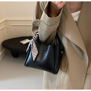 Detail of a black leather bucket bag with a checkered silk scarf on the handle