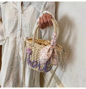 Close-up of hand-woven straw bucket bag with purple hello embroidery and silk scarf handle