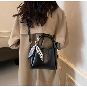 Close-up of black leather bucket bag with fashion stamp and decorative printed silk scarf