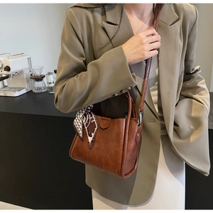 Detail of vintage brown leather bucket bag with silk scarf on minimalist background