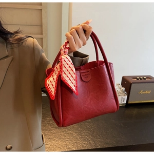 Detail of red textured leather bucket bag with decorative scarf and magnetic closure