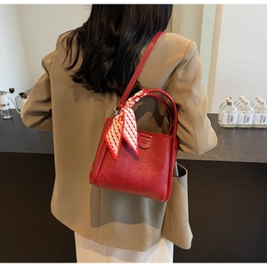 Detail of red leather bucket bag with silk scarf on handle worn as a crossbody bag