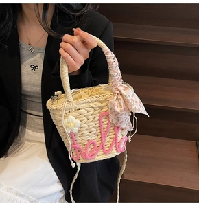 Close-up of woven straw bucket bag with pink hello text and floral scarf handle