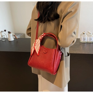 Detail of red bucket bag with silk scarf handle and embossed logo in a cafe setting