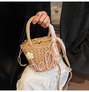 Detail of straw bucket bag with hello embroidery, floral charm and silk scarf handle