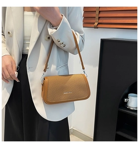 Detail shot of brown woven texture flap shoulder bag worn with a white blazer