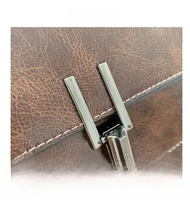 Detail view of brown lychee leather bag featuring a metallic U-shaped buckle and white stitching