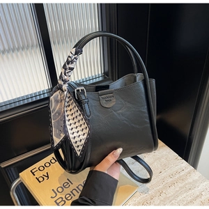 Detail of black vintage bucket bag with elegant silk scarf wrap and textured leather