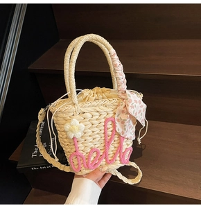 Detail of beige woven straw bag with pink hello text and floral scarf handle