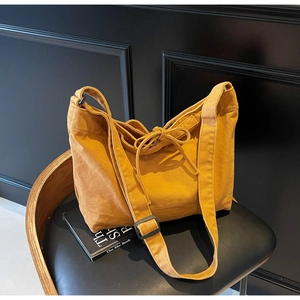 Detail of ginger yellow canvas tote bag with adjustable black buckle on a leather chair