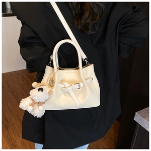 Détail du sac à main beige avec boucle et ours en peluche sur un manteau noir