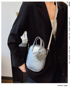 Detail of silver crossbody bag with metallic finish, heart charm and branding on black suit