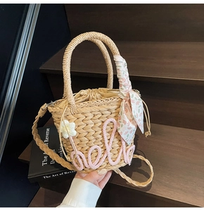 Detail of straw woven bucket bag with hello embroidery and floral scarf on handle