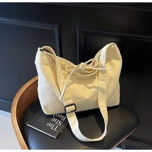 Detailed view of cream canvas tote bag with wide strap and drawstring on a chair