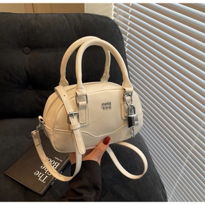 Détail du sac Boston crème avec logo argenté, cadenas et breloque clé décorative