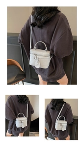 Detail of light grey quilted box crossbody bag with handle and adjustable shoulder strap
