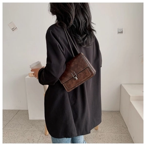 Detail view of a vintage dark brown suede crossbody bag with gold chain and metal buckle