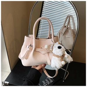 Détail d'un sac à main rose tressé avec un charm d'ours en peluche et une boucle en métal