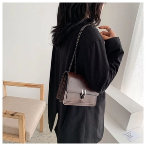 Detail view of brown leather crossbody bag featuring metal chain and organza side folds