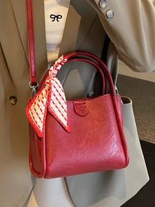 Retro red leather bucket bag with silk scarf handle detail worn by model in olive blazer