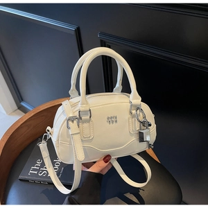 Détail d'un sac Boston blanc crème avec logo en métal argenté et breloque cadenas sur livre
