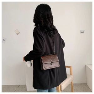 Detail showing deep brown matte leather square bag with silver clasp worn by model