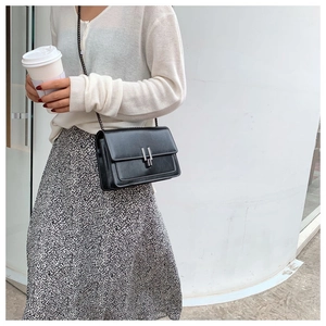 Detail of black crossbody bag with silver buckle and metal chain strap on model