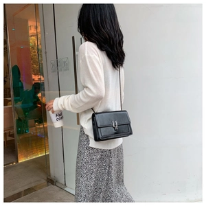 Detail view of black leather crossbody bag with silver H buckle on female model