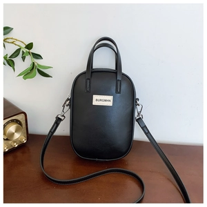 Detail of a minimalist black PU leather mini crossbody bag with rectangular logo on wooden table