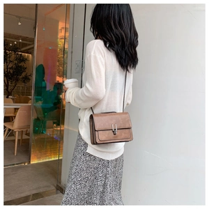 Close-up of brown suede crossbody bag featuring a silver H-shaped metal buckle and chain