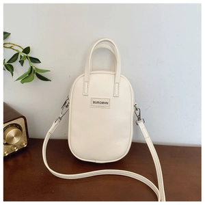 Detail of a white oval crossbody bag with top handle and BURGMHN logo on a wooden desk