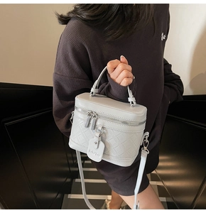 Detail of light gray quilted box bag with dual zippers and leather texture handle