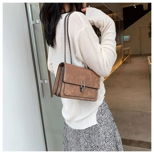 Macro view of brown leather crossbody bag featuring vintage chain and metallic bar lock