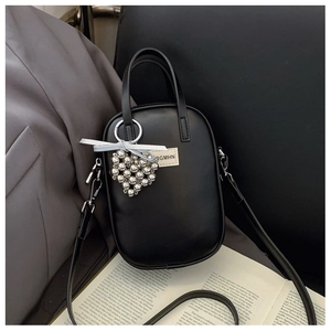 Detail of minimalist black oval crossbody bag with silver heart charm and textile label