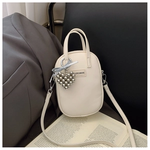 Close-up of beige crossbody bag with heart bead pendant and blue ribbon bow detail