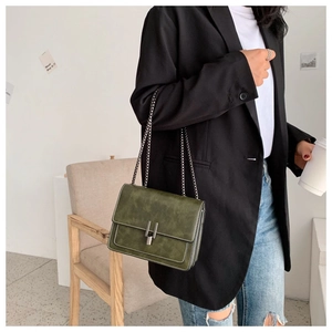 Detail of dark green matte crossbody bag with silver buckle on a stylish model